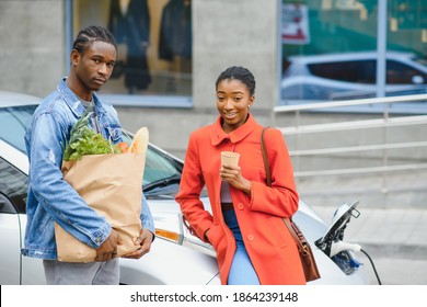 Happy Young Adult African American Man And Smiling Woman Charging Electric Car.