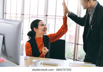 Happy young adult asian business people with technology concept. Woman hi five with team for work has success. Workplace table with computer. Minimal office style with window light on day.