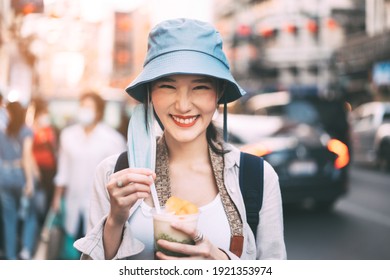 Happy young adult asian foodie woman backpack traveller eating asia dessert. People traveling with new normal lifestyle at outdoor at China town street food market. Bangkok, Thailand