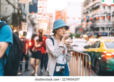 Happy young adult asian foodie woman backpack traveller eating asia dessert. People traveling with lifestyle outdoor at China town street food market. Bangkok, Thailand