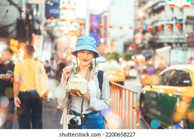 Happy Young Adult Asian Foodie Woman Backpack Traveller Eating Coconut Juice. People Traveling With Lifestyle Outdoor At China Town Street Food Market. Bangkok, Thailand