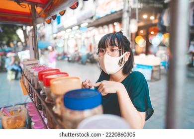 Happy Young Adult Asian Foodie Woman Order Vendor Asia Dessert. Wear Face Mask. People Traveling With New Normal Lifestyle At Outdoor Street Night Food Market.