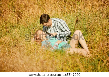 Happy young adult couple in love on the field. Two,  man and woman smiling and resting on the green grass.