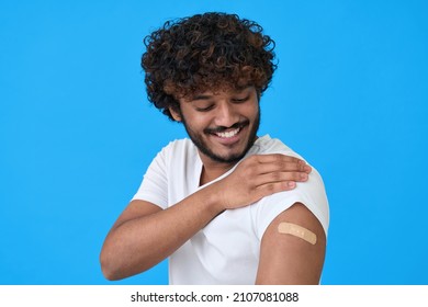 Happy Young Adult Indian Latino Man Showing Bandage Plaster On Arm After Getting Vaccination Isolated On Blue. Vaccine And Inoculation, Immunization Campaign For Covid Flu Prevention Concept.