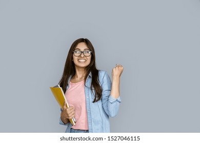 Happy Young Adult Indian Woman Winner Celebrate University Admission Scholarship Good Test Exam Result. Student Girl Hold Copybook Looking At Camera Standing Isolated On Grey Background Copy Space