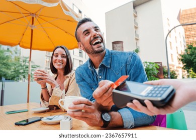 Happy young adult man paying the bill with a contactless credit card on a restaurant, bar or coffee shop. Handsome male smiling holding a creditcard and giving a payment transaction to the cashier