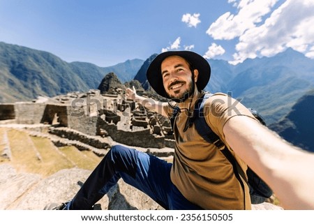 Happy young adult man taking selfie portrait in Machu Picchu. Joyful traveler enjoying vacation visiting Peru. South american travel holidays concept.