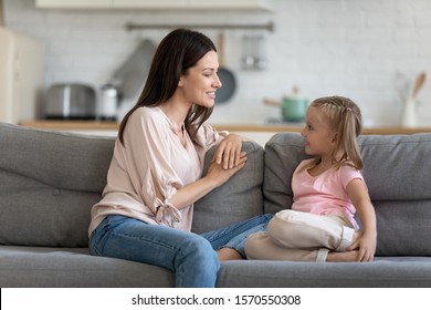 Happy Young Adult Mother And Cute Child Enjoy Talking Relaxing Sit On Sofa, Understanding Mom Friend Having Sincere Conversation With Little Daughter At Home, Trust In Parent Kid Relationship Concept