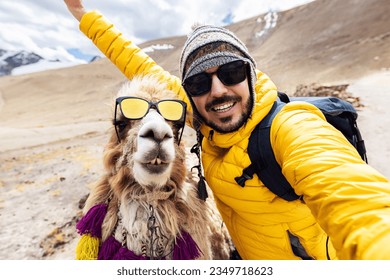 Happy young adult traveler taking selfie with cute peruvian llama in Peru. Funny self portrait of joyful smiling tourist hiker enjoying vacation in South America. Travel and holidays concept