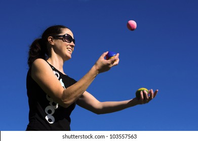 Happy young adult woman juggler is juggling balls in the air isolated against blue sky background.  Concept photo of women power, success and control.Real People. Copy space