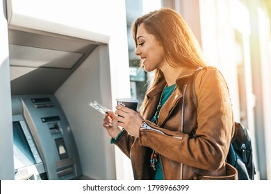 Happy young adult woman standing in front of ATM machine, smiling and holding credit or debit card.  - Shutterstock ID 1798966399