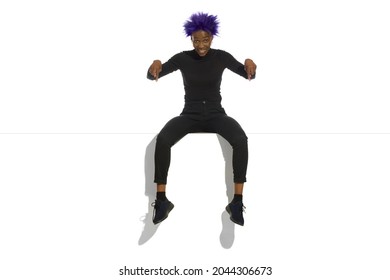 Happy young african america woman with short purple hair is sitting on a top of a banner and pointing down. Full length studio shot. - Shutterstock ID 2044306673