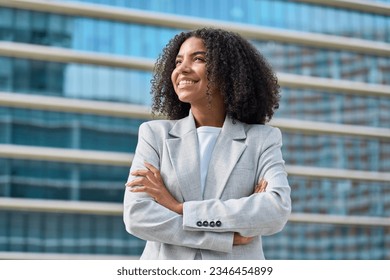 Happy young African American business woman standing in city looking away. Confident smiling confident professional businesswoman leader wearing suit thinking of success, dreaming of new goal outdoor.