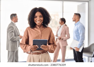 Happy young African American business woman standing in office lobby. Smiling confident professional female company employee leader manager holding tablet looking at camera. Portrait. - Powered by Shutterstock