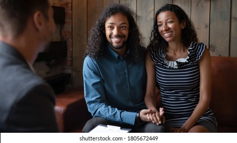 Happy Young African American Couple Holding Hands, Sitting On Couch At Meeting With Realtor, Buying Real Estate, Planning Wedding With Agent, Family Visiting Psychologist, Good Relationship