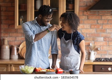 Happy young African American couple have fun preparing healthy delicious vegetarian food at home kitchen. Smiling biracial man and woman family tenants enjoy cooking vegan diet breakfast together. - Powered by Shutterstock