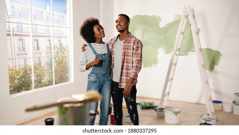 Happy Young African American Couple Stands In Room In New Own Apartment Discussing Design And Decor Of House. Wife Talking To Husband About Home Repair. Renovation And Improving Apartment Concept