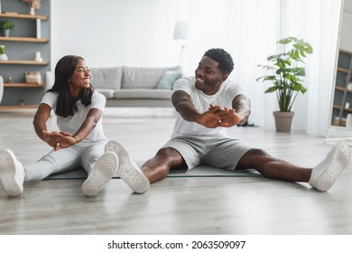 Happy young African American couple stretching sitting on floor yoga mats, making domestic workout, doing flexibility exercises at home. Fit black guy and his girlfriend training in living room - Powered by Shutterstock