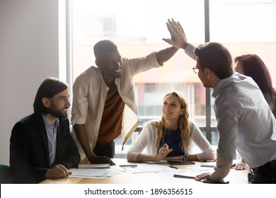 Happy young african american employee giving high five to smiling 30s male team leader at colleagues group brainstorming meeting, celebrating successful project finish or sharing corporate success. - Powered by Shutterstock