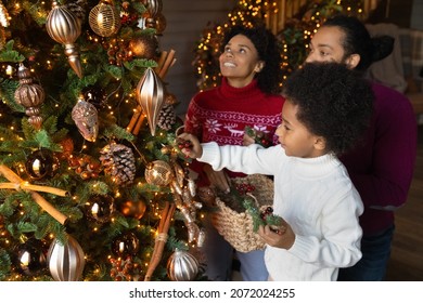 Happy Young African American Family With Small Son Decorate Christmas Fir Tree At Home Together. Smiling Parents With Boy Child Prepare For Winter Holidays Celebration. Unity, New Year Concept.