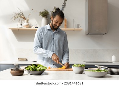 Happy young African American food blogger man preparing dinner in kitchen, slicing vegetables at table with fresh ingredients, lettuce, dish, enjoying cooking healthy vegan, vegetarian meal - Powered by Shutterstock