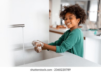 Happy young African American girl washing hands with soap smiling and looking at camera while standing at kitchen sink. - Powered by Shutterstock