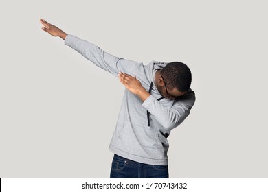 Happy young african american guy in sportswear performing show dance, making dab move gesture. Cheerful black millennial man presenting popular internet meme pose, isolated on grey studio background.