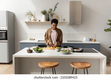 Happy young African American housewife girl slicing fresh vegetables for salad in home kitchen, preparing dinner from organic food ingredients, enjoying cooking hobby, keeping healthy eating - Powered by Shutterstock