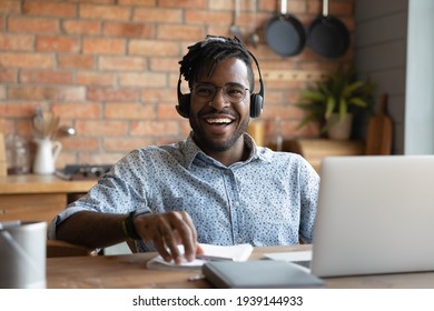 Happy Young African American Man In Eyewear And Modern Headset Sitting At Table With Computer, Laughing Distracted From Distant Study Or Remote Job, Having Fun Entertaining Feeling Joyful At Home.