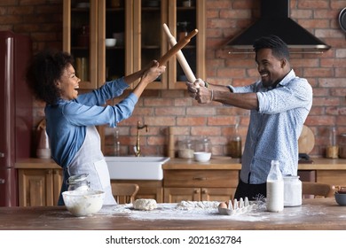 Happy Young African American Man And Woman Spouses Have Fun Fight On Kitchen Appliances Cooking Together At Home. Smiling Millennial Ethnic Couple Laugh Baking Preparing Food. Hobby Concept.