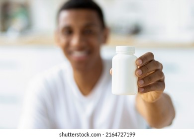 Happy young african american man holding capsules and open bottle. Painkiller, headache medication or vitamins concept