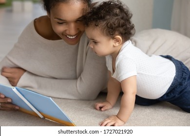 Happy young african American mom and little baby toddler relax at home bed reading children book together, smiling loving biracial mother and small infant child enjoy family weekend, childcare concept