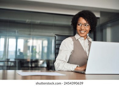 Happy young African American professional business woman bank worker or hr manager, corporate employee looking away at work working on laptop computer in office thinking of future career. Copy space. - Powered by Shutterstock