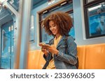 Happy young African American woman passenger smile and using smart mobile phone in subway train station.