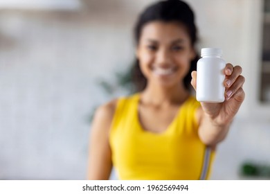Happy young African American woman holding bottle of dietary supplements or vitamins in her hands. Healthy lifestyle concept
