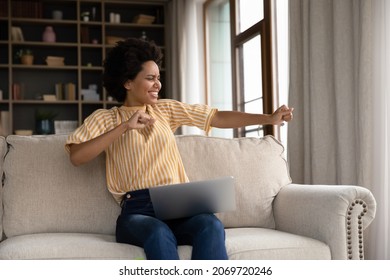 Happy young African American woman dancing to music or stretching muscles enjoying break pause time working remotely on computer at home, celebrating finishing workday, having fun alone in living room