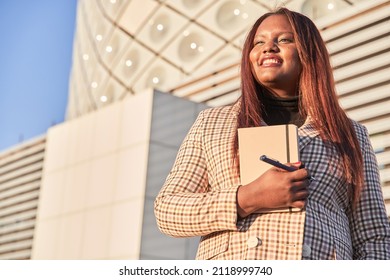 Happy Young African American Woman With Notebook In Hands Standing Outside Office And Smiling. Portrait Of Successful Business Professional, Company Employee, Business Woman Or Financial Advisor.