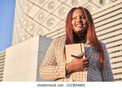 Happy Young African American Woman With Notebook In Hands Standing Outside Office And Smiling. Portrait Of Successful Business Professional, Company Employee, Business Woman Or Financial Advisor.