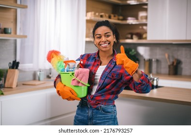 Happy young african american woman in rubber gloves with bucket of cleaning supplies show thumb up, approving cleaning at modern kitchen interior. Housework, hygiene and housewife at home due covid-19 - Powered by Shutterstock