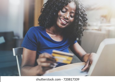 Happy Young African American Woman Shopping Online Through Laptop Using Credit Card At Home. Horizontal,blurred Background.Cropped