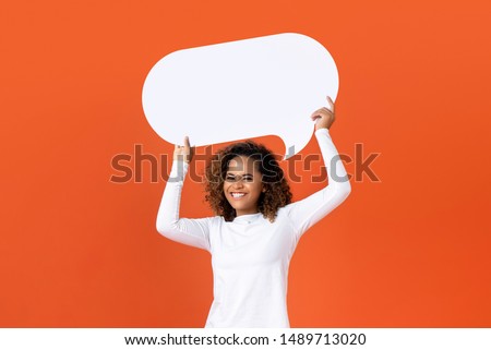 Happy young African American woman in plain white long sleeve t-shirt holding empty speech bubble isolated on orange  background