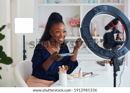 happy young african american woman streaming a beauty vlog from home, online content creator applying a makeup on