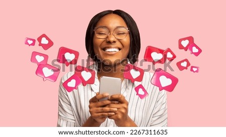 Happy young african american woman has romantic chat with hearts on phone, enjoys message, good news, communication on pink studio background, panorama. App for relationships and love, dating remotely