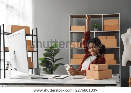 Happy young African Americans woman entrepreneur, Smile for sales success after checking order from online shopping store in a smartphone at home. Concept of merchant business online and e-commerce