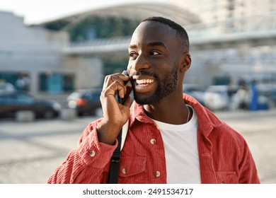 Happy young African Black man hipster or tourist with backpack standing on city street outdoors holding smartphone talking on mobile cell phone having conversation making call on smartphone. - Powered by Shutterstock