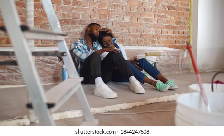 Happy Young African Couple Relaxing After Painting Room In New House On Floor. Cheerful Afro Girlfriend And Boyfriend Sitting On Floor Discussing Apartment Redecoration Plan