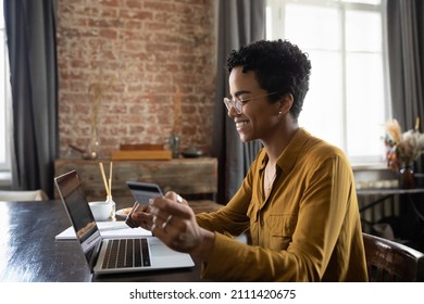 Happy young African customer woman using laptop and credit card for online shopping. Cheerful shopper making payment for purchase on Internet, transactions, mortgage fees, buying on stores websites