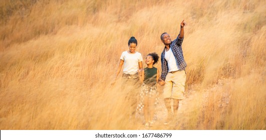 Happy young African family father, mother and daughter hiking and holding hands together with smiling face. Relaxing family  parents and child walking together on golden meadow on mountain - Powered by Shutterstock