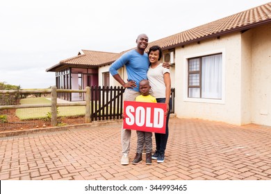 Happy Young African Family In Front Of Their Home With Sold Real Estate Sign