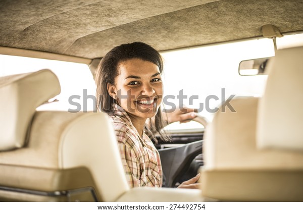 happy young african girl driver inside old retro\
vintage car Cute woman look back at pasangers with smiley face idea\
taxi driver against sunset Light shine sky Concept of exam Vehicle\
- second home